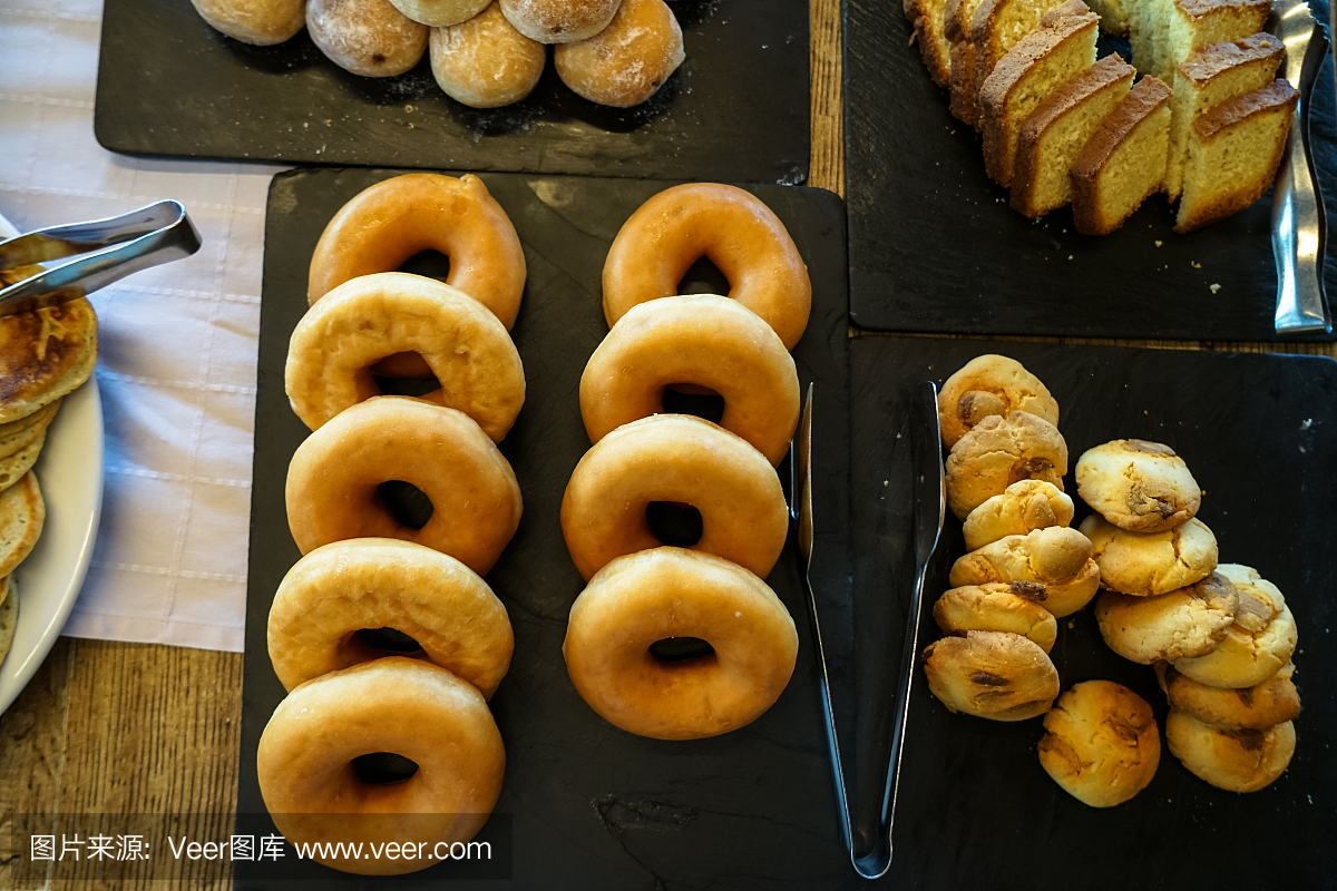 希腊自助早餐桌上有一盘盘的甜烘焙甜点,包括甜甜圈、饼干、奶油蛋糕、小面包等